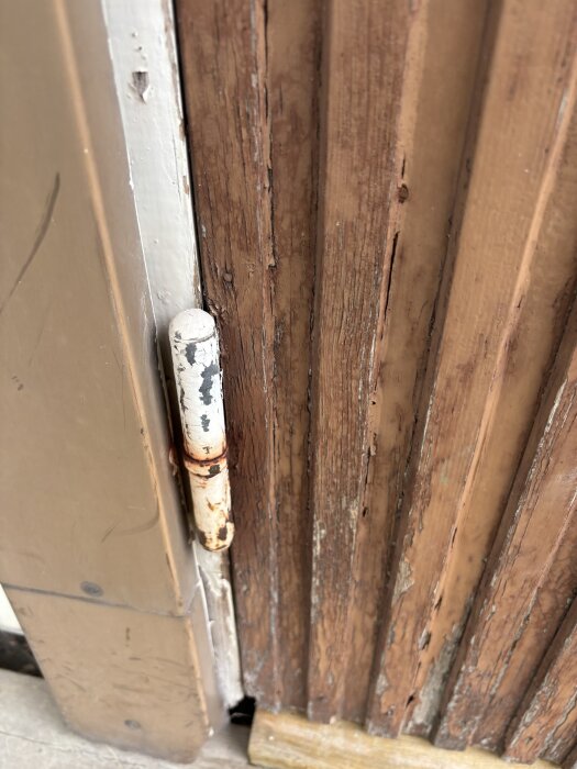 Gammal dörr med rostiga gångjärn och sliten träyta, detaljer av dörrkarm och skador synliga.