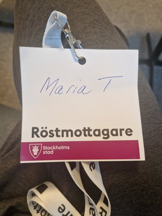 Namnskylt för röstmottagare från Stockholms stad, med ett handskrivet namn och en snodd med klämma.