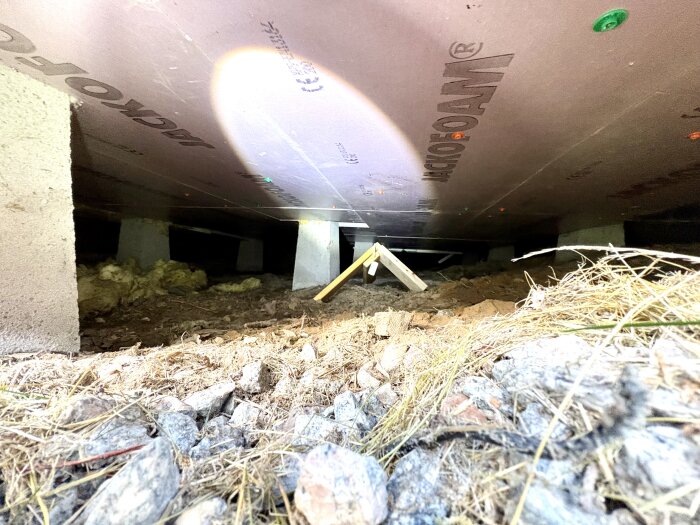 Krypgrund med grus och isolering under hus på plintgrund, sedd nedifrån med inspekterbar isolering och undergolv.