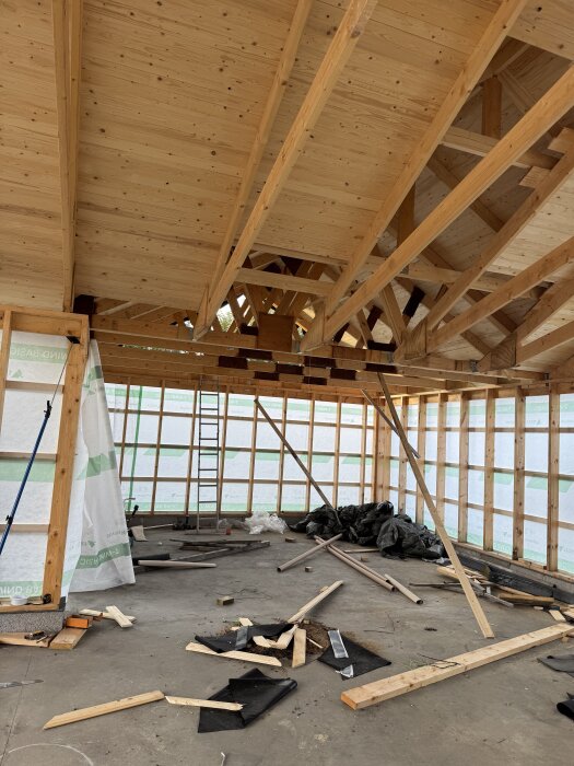 Inre skelett av garage under konstruktion med träbalkar i taket och byggmaterial på golvet.