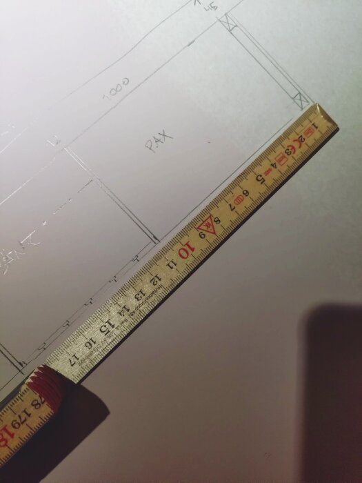 Skiss på ett byggprojekt med måttangivelser och en tumstock som mäter 17 cm på ett papper där ordet "PAX" syns.