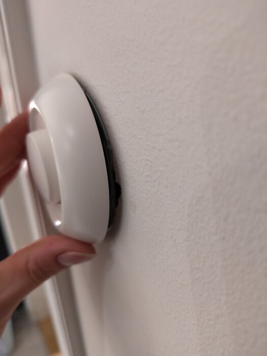 Vit dimmer med lossnad övre del på vägg, hålls av en hand.
