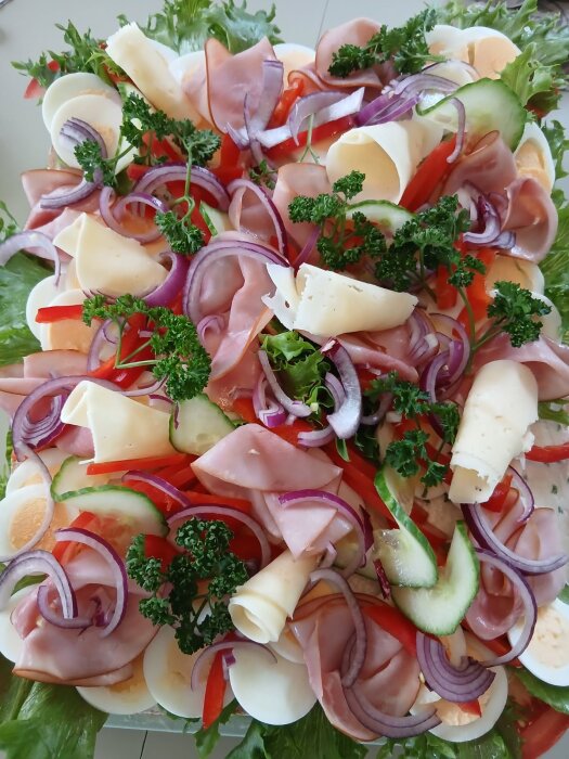 Smörgåstårta utan räkor, pyntad med skinka, ost, ägg, rödlök och persilja, på en bädd av sallad.