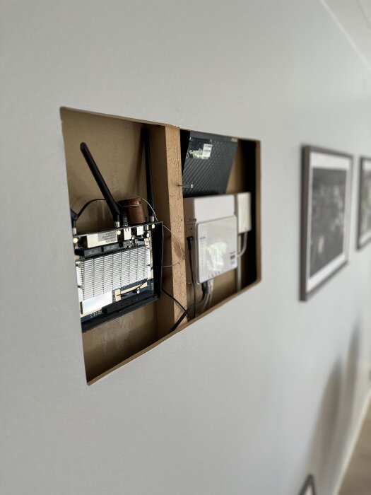 Inbyggd router i vägg med öppet lock för bättre kylning, omgiven av träram och ledningar.
