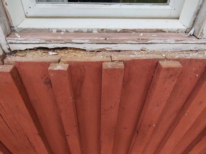Ruttna trädelar vid fönsterkarmens nedre kant där fönsterbrädan tagits bort, synlig springa och skador på rödmålad yttre panel.