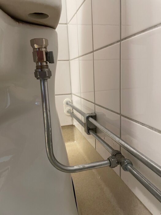 Flexibelt rör och t-koppling bakom en IFÖ Cera toalett mot en kaklad vägg.