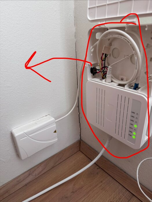 Fiberbox monterad på vägg med en blå kontakt och kablar, röd pil pekar mot en annan vägg för eventuell flytt.