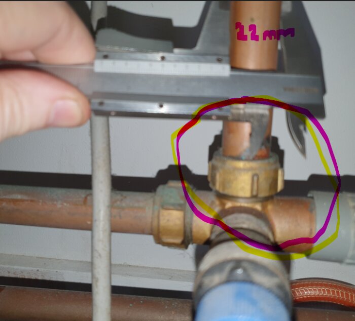 Hand håller ett skjutmått mot ett kopparrör i en VVS-installation. Markering visar rördiameter 22 mm.