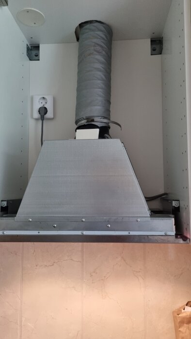 Fläkt installerad i köksskåp med ventilationsrör och elkontakt.