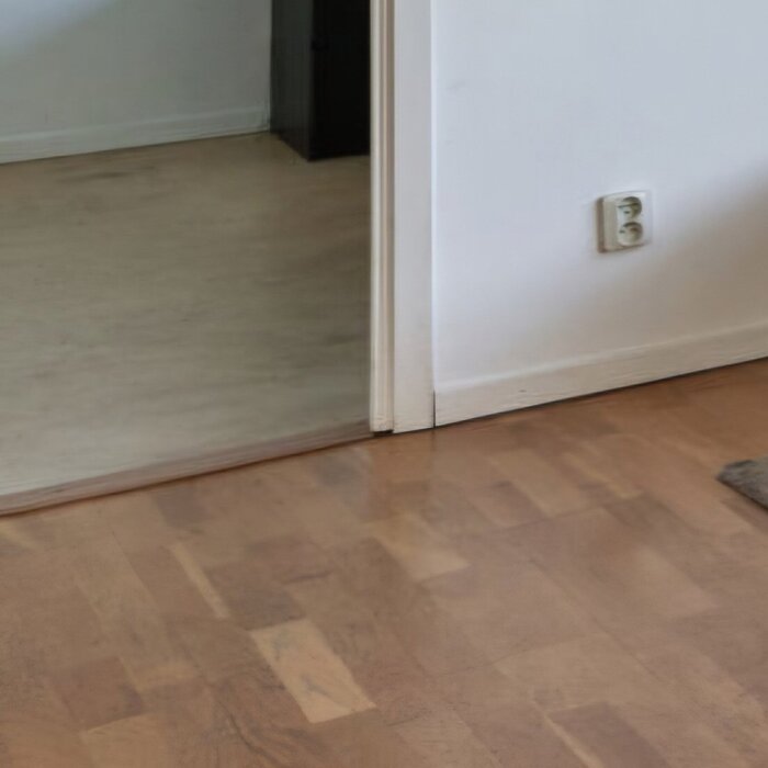 Rummet visar golv av 3-stavsparkett som sträcker sig över två rum, med en dörröppning däremellan, och en vägguttag synligt.