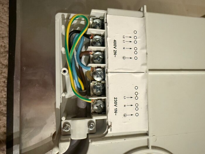 Elektrisk anslutningsplint på spis med märkningar och flera anslutna kablar i olika färger för 400V och 230V system.