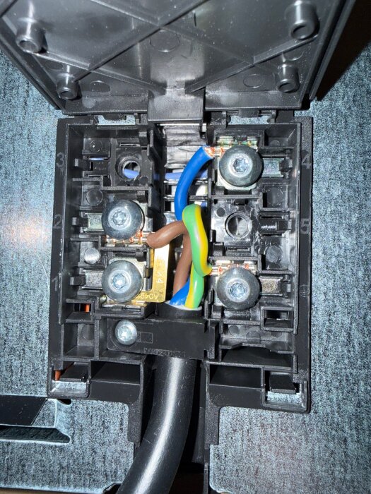 Elektrisk kopplingsbox med skruvterminaler, färgade kablar och nummer märkta på insidan, använd i diskussion om spiskopplingar.