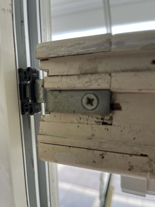 Gammal fönsterhake av metall med rostiga skruvar, monterad på en träram.