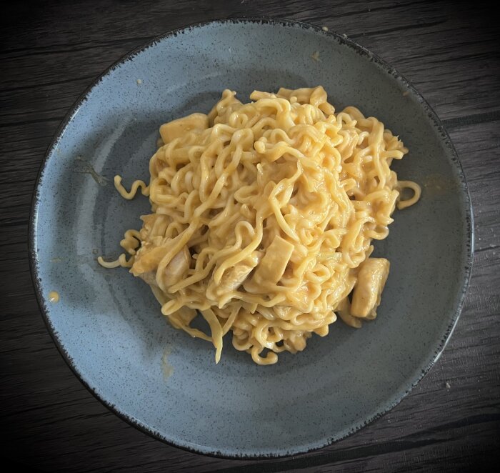 Kycklinggryta med nudlar, kokosmjölk och curry på en grå tallrik.