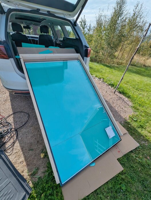 Glasrutor liggande i bakluckan på en bil, skyddade av en ram och skivor, redo för transport, med gräs och träd i bakgrunden.