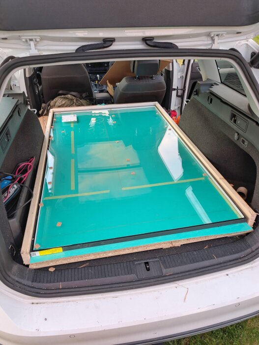 Bilens bagageutrymme visar en ram med glasrutor, packade med grönt foam och golvspånskivor för transport.