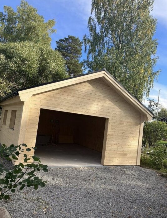 Isolerat 30 kvm trädgarage utan el, port och fönster, placerat på en grusad yta med omgivande träd.