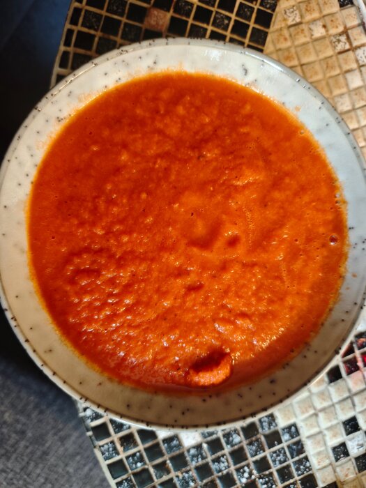 Skål med hemlagad tomatsoppa gjord på egna tomater, foto ovanifrån på ett mosaikbord.