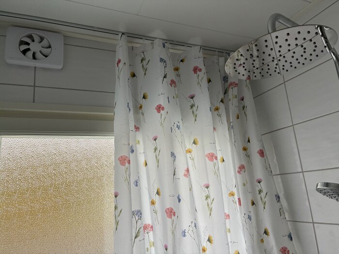 Duschdraperi med blommönster hänger på en takskena bredvid en dusch och ventil i ett badrum.