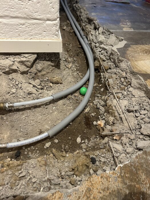 Byggarbetsplats med uppbilad golv där elementrör har exponerats och en grön boll ligger bredvid rören i den öppna konstruktionen.