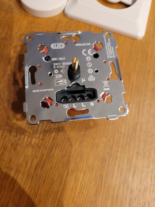 Dimmer för väggmontering, märkt ELKO, med kontakter för elanslutning, placerad på ett träbord.