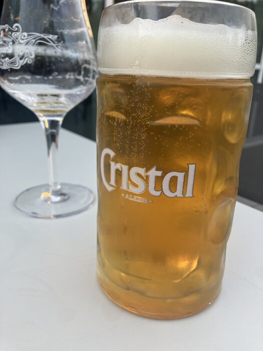 Ett fullt glas med öl bredvid ett tomt vinglas på ett bord.
