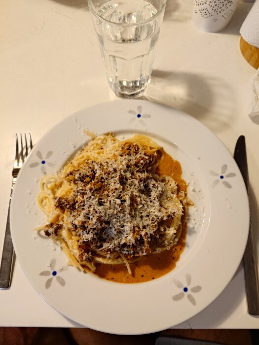 Tallrik med spaghetti toppad med köttfärssås och riven parmesan. Bredvid står ett glas vatten.