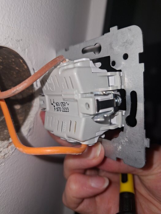 Närbild på en elektrisk väggströmbrytare som hålls av en person; visar ledningar och brytarkonfiguration.