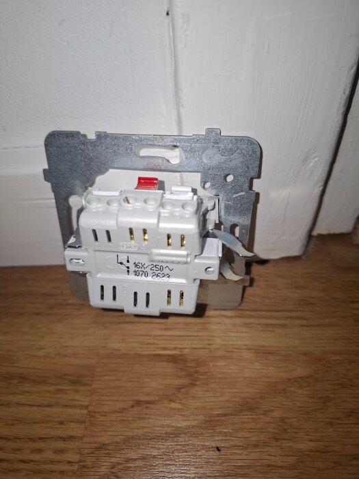 Väggströmbrytare monterad utan ram, sedd mot en vitmålad träpanel och golv av trä.