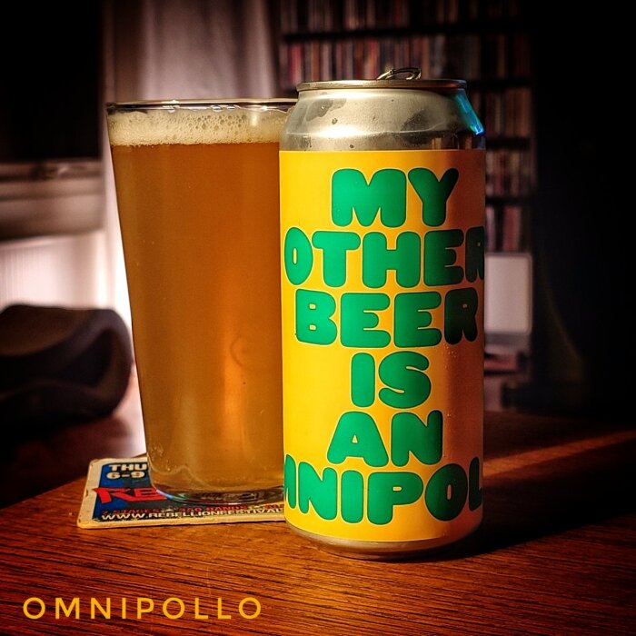 En öl i glas bredvid en ölburk med texten "My Other Beer Is An Omnipollo" på ett bord.