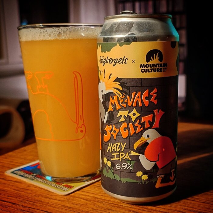 En glas med ljus öl bredvid en burk med etiketten "Menace to Society" Hazy IPA, 6.9%, från Stigbergets x Mountain Culture.