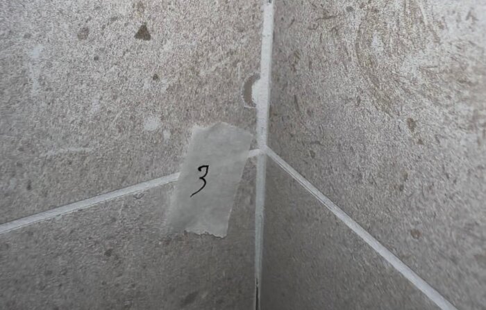 Flisa på granitkeramikplatta i hörnet av ett badrum med tejp markerad "3".