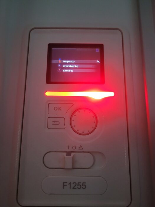 Panel med display och knappar, märkt F1255, visar menyval: temperatur, schemaläggning och avancerat. Röd belysning vid sidan om kontrollpanelen.