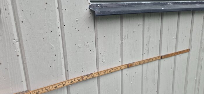 Fasad av garage med svarta småprickar och en tumstock mot väggen för referens.