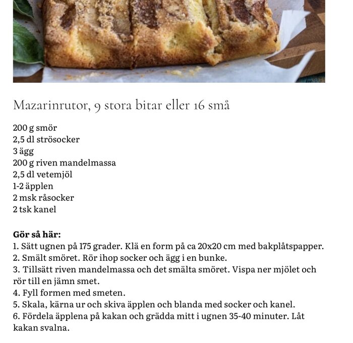 Mazarinruta med äpple och kanel på bakplåtspapper. En gyllenbrun kaka, delad i bitar, med synliga äppelskivor och ett lager kanelsocker ovanpå.