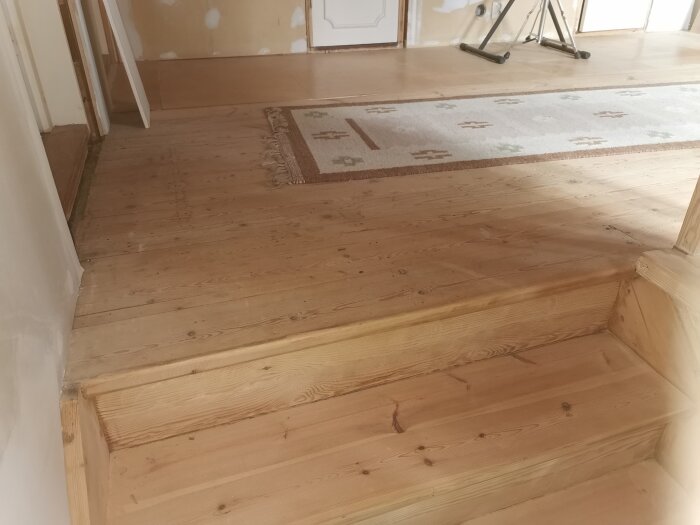 Översta trappsteget och golvet i trä med en matta vid en trappa i ett rum under renovering.