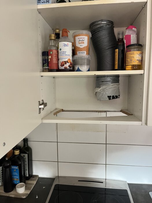 Öppet köksskåp med matvaror och en fläktkanal, utrymme för fläkt ovanför en spishäll syns.