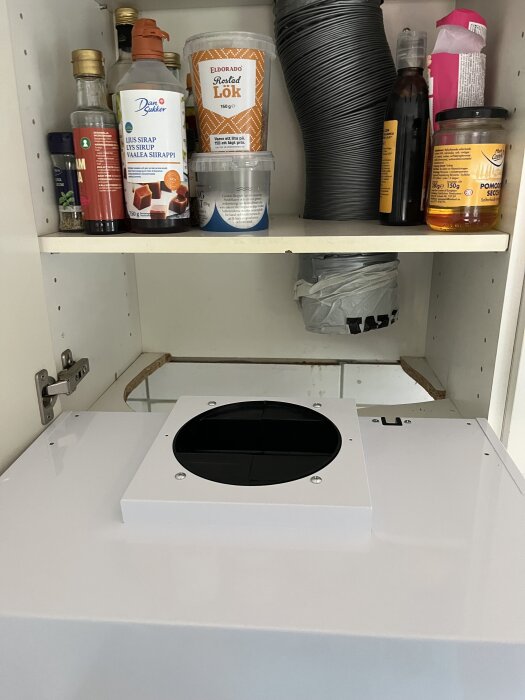 Inbyggnad av köksfläkt i ett 50 cm brett skåp med dörrgångjärn som förhindrar installation, omgivna av matvaror och hushållsföremål.