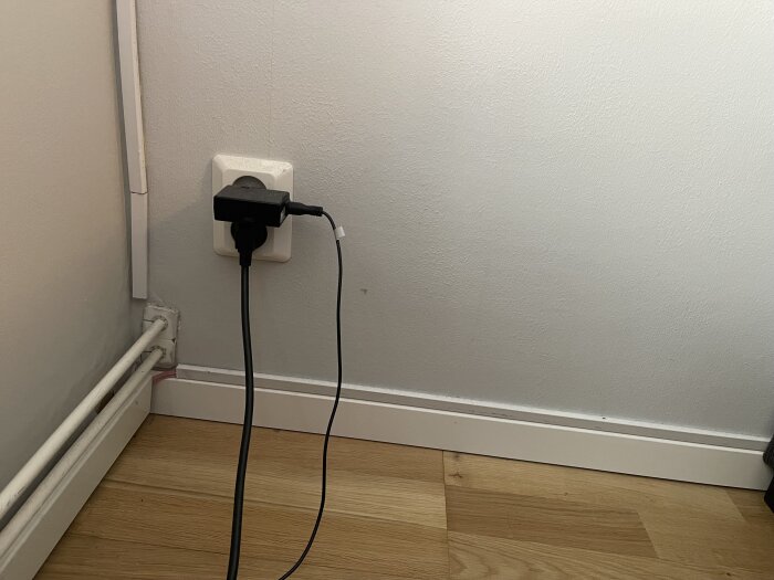 Power outlet on a concrete wall with plugged-in cables, located near a white baseboard, over a wooden floor.