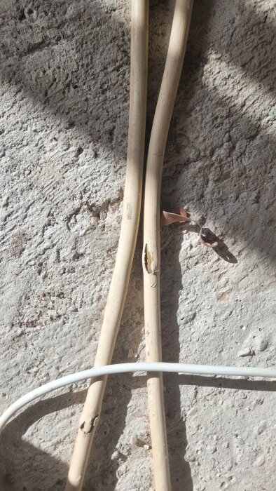 Skadade elkablar på en grov cementvägg, en av kablarna har en synlig reva i isoleringen.