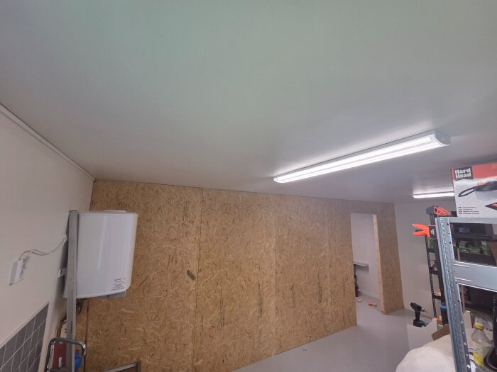 Garage med skivbeklädda väggar, hyllor med förvaringslådor och verktyg. Vägguttag, lysrör och tegelvägg syns.