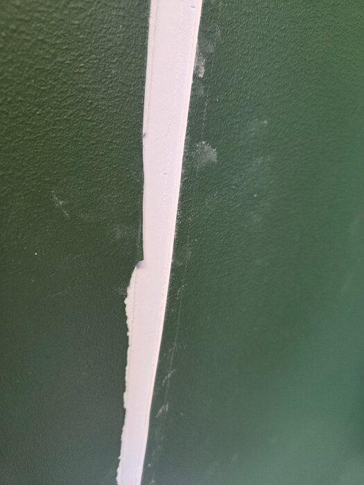 Spricka i mörkgrön vägg där skarvremsa har släppt, vilket skapat en ojämnhet i ytan.