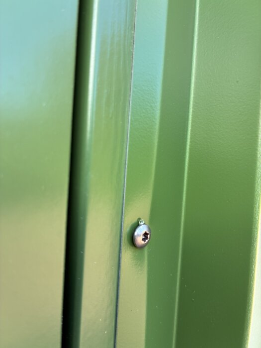 Grönlackad plåt med skruv som sitter snett, visar skador och ojämnheter efter installation vid dörrkarm, troligen orsakade av plåtslagaren.
