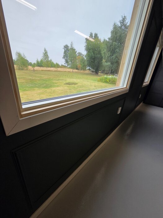 Fönster med nyligen ommålade foder i samma kulör som väggarna, utsikt mot trädgård utanför, och epoximålat golv inomhus.