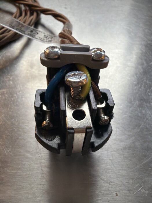 Elkontakt med blå och gulgrön kabel ansluten med spårskruv på metallisk yta.