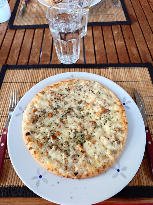 Pizza med kantareller serverad på en tallrik på träbord, tillsammans med ett glas vatten.