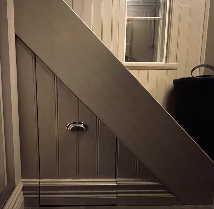 Låda under snedtak med pärlspontfront och en kromad handtagsdetalj, integrerad med rummet genom en matchande sockel.