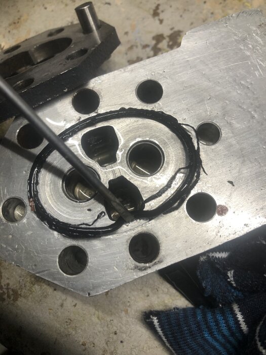 Metallplatta med o-ring och hål, möjlig ventilhusdel. Verktyg pekar mot området.
