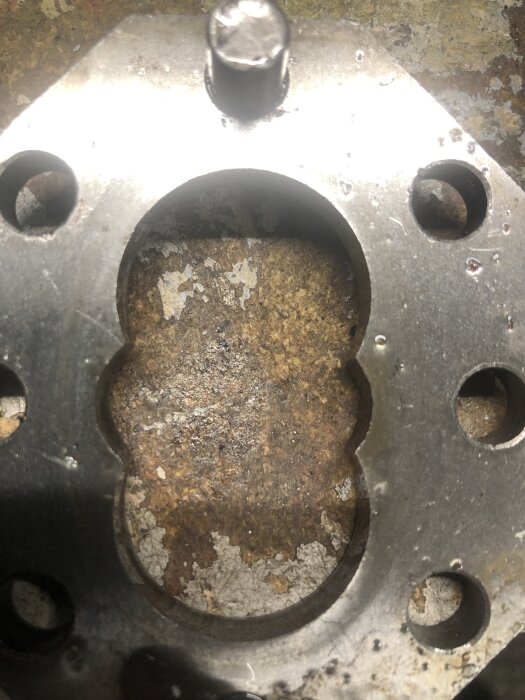 Metallplatta med ovala och runda hål, del av mekaniskt system. Slitningar och korrosion synliga på plattans yta.