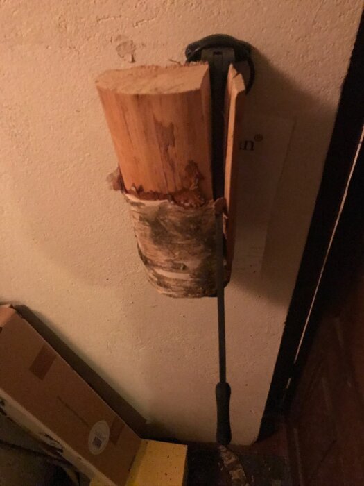 Ett vedträ fastsatt i en väggmonterad vedklyv av märket Stikkan, monterad på en vägg i ett nybyggt hus av hampakalk.